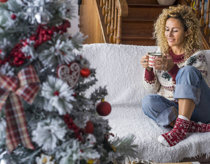 Lächelnde junge Frau hält eine Kaffeetasse, während sie zu Hause auf dem Sofa sitzt - SIPF02426
