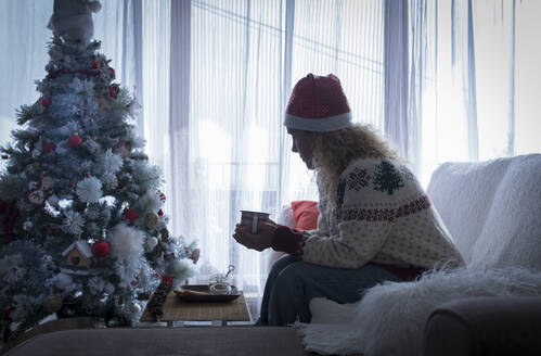 Frau trinkt Kaffee, während sie zu Hause auf dem Sofa sitzt, während Weihnachten - SIPF02433