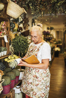Blumenhändlerin prüft Pflanzen und schreibt in ein Buch im Geschäft - GRCF00994