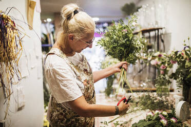 Blumenhändlerin schneidet Pflanzenstängel bei der Arbeit im Blumenladen - GRCF01000