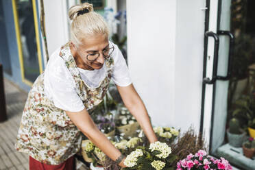 Blonde Blumenhändlerin arrangiert Blumen vor dem Geschäft - GRCF01003