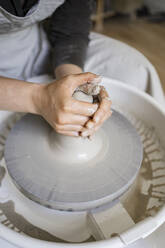 Young female potter molding clay on pottery wheel in workshop - RCPF01307