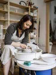 Smiling craftswoman with pottery wheel working in workshop - RCPF01309