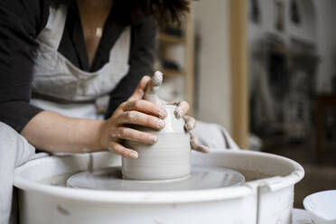 Craftswoman molding clay on pottery wheel in workshop - RCPF01314