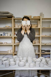 Töpferin bedeckt Gesicht mit Keramik in der Werkstatt - RCPF01322