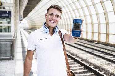 Happy man showing vaccination qr code on smart phone screen at subway platform - UUF24717