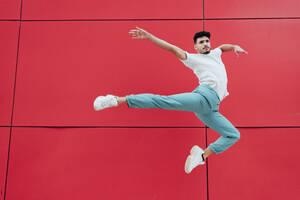 Männlicher Turner tanzt vor einer roten Wand - MIMFF00723