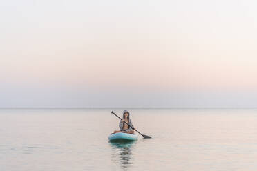 Boy paddleboarding on sea during sunset - EYAF01772