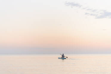 Junge mit Ruder Paddleboarding auf dem Meer bei Sonnenuntergang - EYAF01773