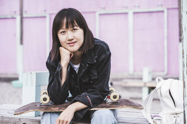 Teenage girl with skateboard sitting on bench - UUF24721