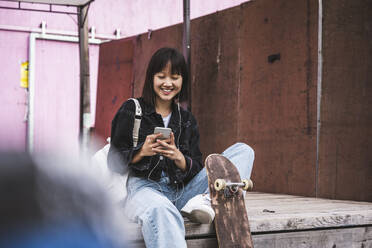 Teenage girl using smart phone while sitting on boardwalk - UUF24729