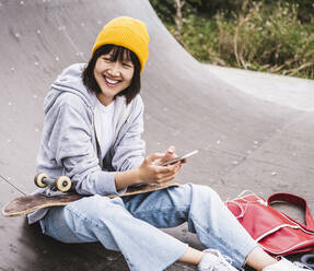 Glücklicher weiblicher Teenager mit Mobiltelefon im Skateboard-Park - UUF24743