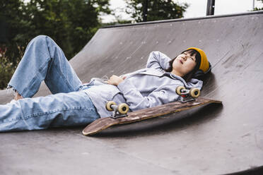Female teenager with hand behind head resting on sports ramp - UUF24744