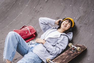 Teenage girl listening music through wireless headphones at skateboard park - UUF24745