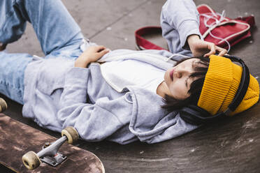Teenage girl wearing wireless headphones resting at skateboard park - UUF24746