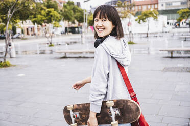 Glücklicher weiblicher Teenager mit Skateboard auf dem Gehweg - UUF24752