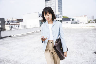 Female professional with briefcase using mobile phone on rooftop - UUF24760