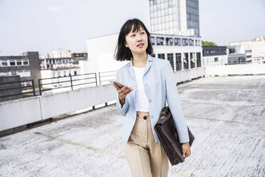 Weiblicher Geschäftsmann mit Mobiltelefon und Aktentasche auf einem Dach - UUF24761