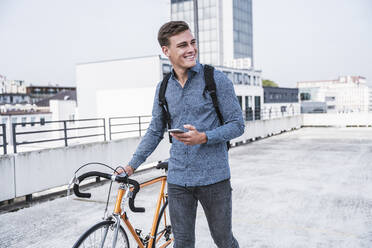 Junger Mann mit Fahrrad auf dem Dach eines Parkhauses - UUF24767