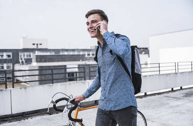 Glücklicher junger Mann mit Fahrrad, der mit seinem Smartphone telefoniert - UUF24769