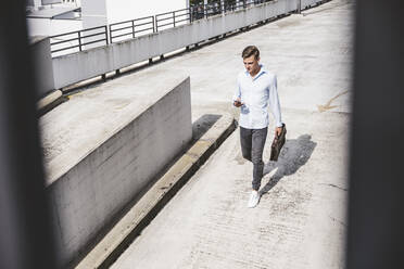 Businessman with briefcase using smart phone while walking on rooftop - UUF24780