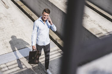 Smiling businessman with briefcase talking on mobile phone - UUF24781