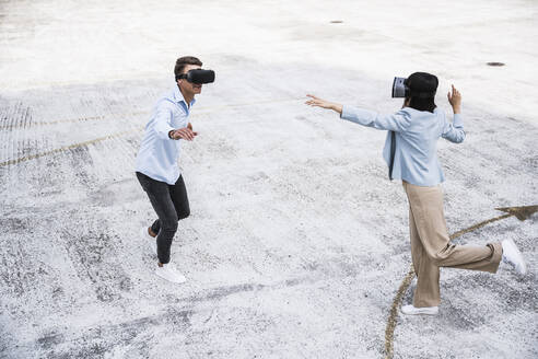 Male and female colleagues using virtual reality headset on rooftop - UUF24788