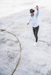 Junger Mann mit erhobener Hand und Virtual-Reality-Headset auf einem Dach - UUF24790
