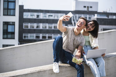 Glückliche männliche und weibliche Freunde nehmen Selfie durch Smartphone während sonnigen Tag - UUF24803