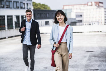 Lächelnde Geschäftsfrau geht mit einem männlichen Kollegen auf einem Dach spazieren - UUF24822