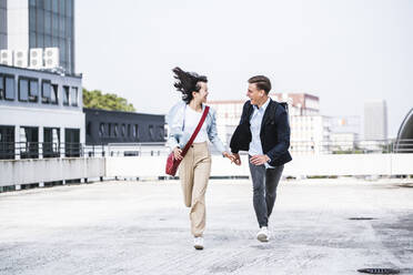 Happy male and female business colleagues running on parking garage rooftop - UUF24826