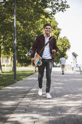 Man with skateboard walking on footpath - UUF24832