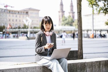 Geschäftsfrau mit Laptop und Smartphone in der Stadt - UUF24842