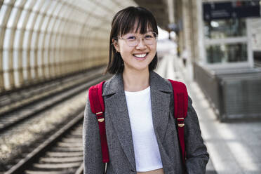Lächelndes jugendliches Mädchen mit Rucksack am Bahnhof - UUF24848