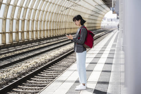 Jugendliches Mädchen mit Rucksack benutzt Handy am Bahnhof - UUF24849