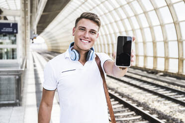 Smiling man showing smart phone at train station - UUF24857