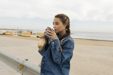 Young woman drinking coffee while standing by railing - VABF04395