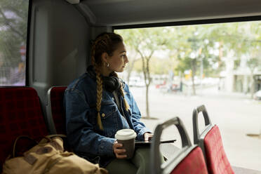 Junge Frau mit digitalem Tablet schaut durch das Busfenster - VABF04399