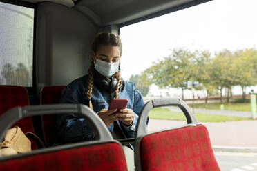 Woman wearing protective face mask using smart phone in bus - VABF04404