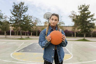 Young woman holding basketball at sports court - VABF04407