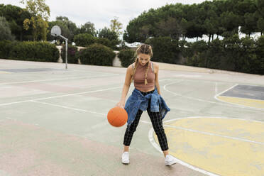 Frau spielt mit Basketball auf Sportplatz - VABF04410