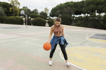 Woman playing with basketball at sports court - VABF04410