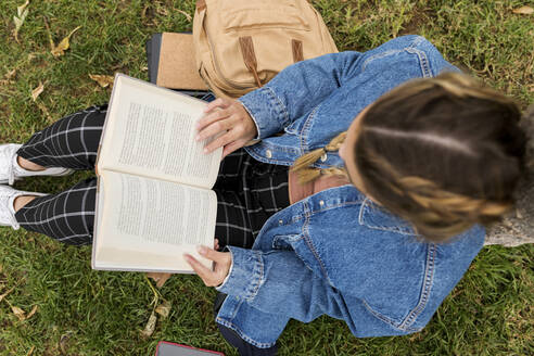 Frau liest ein Buch, während sie im Park im Gras sitzt - VABF04413