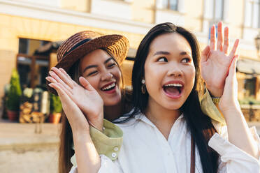 Surprised woman with playful female friend wearing hat - OYF00525