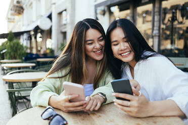 Glückliche Freundinnen benutzen Smartphones in einem Straßencafé - OYF00545