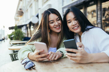 Freundinnen benutzen Mobiltelefone, während sie in einem Straßencafé sitzen - OYF00546