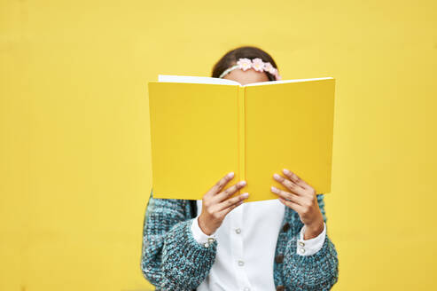 Junge Frau liest gelbes Buch an der Wand - KIJF04138