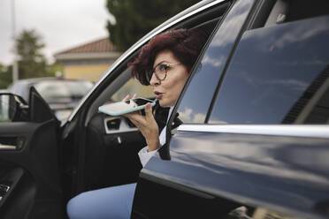 Reife Geschäftsfrau, die im Auto sitzend über einen Lautsprecher mit ihrem Smartphone spricht - JCCMF04047