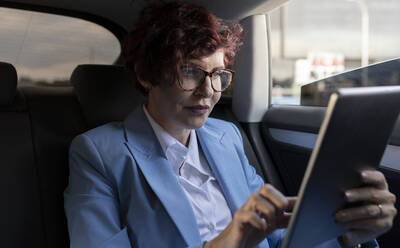 Mature businesswoman using digital tablet while sitting in car - JCCMF04049