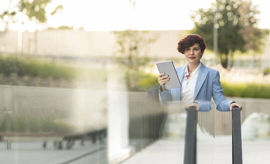 Businesswoman with short hair holding digital tablet by glass railing - JCCMF04061